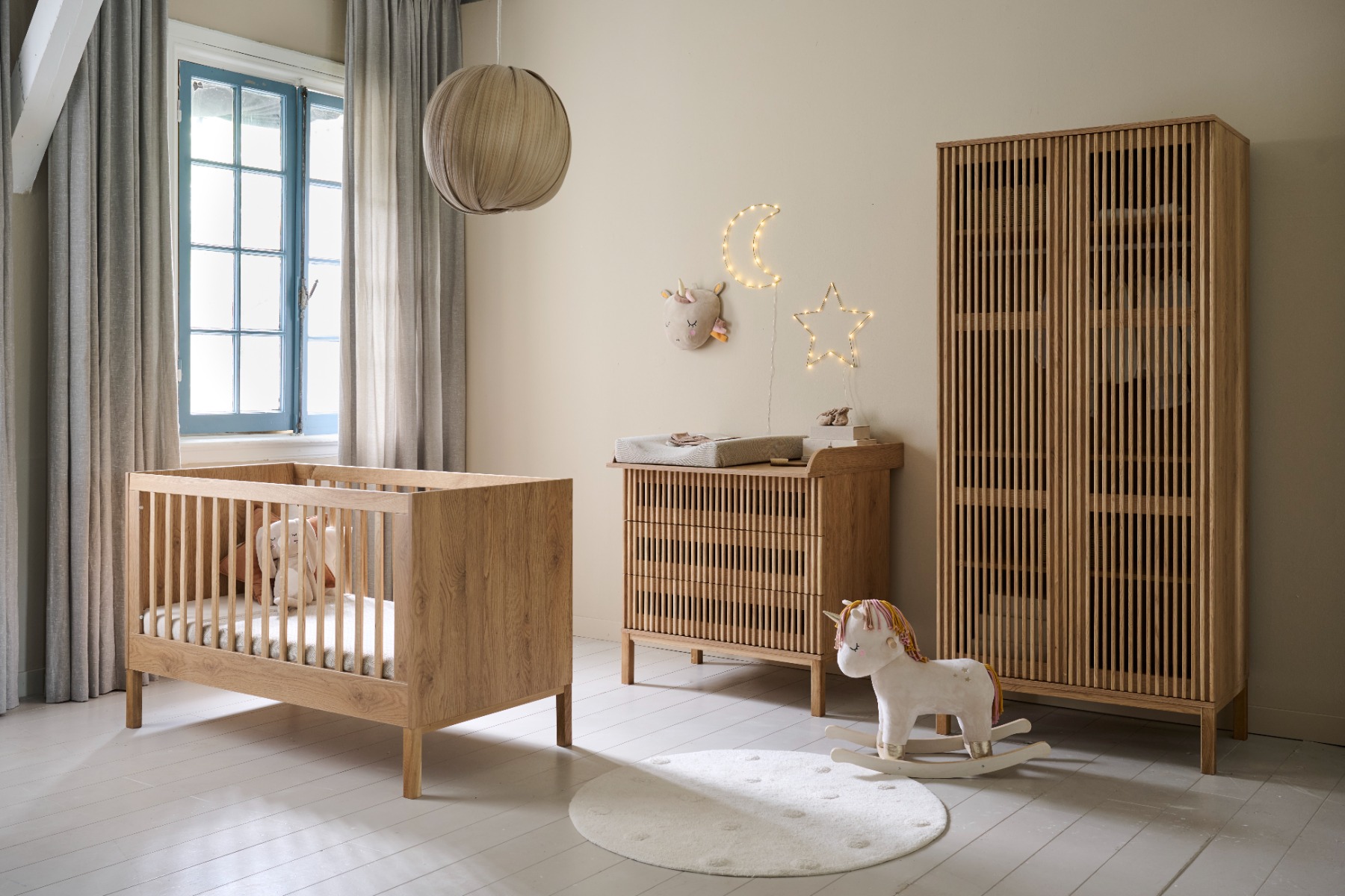“Chambre bébé complète en bois style Japandi avec lit à barreaux en chêne, commode à langer et grande armoire assortie, décorée d’une guirlande lumineuse lune et étoile et d’un cheval à bascule licorne.