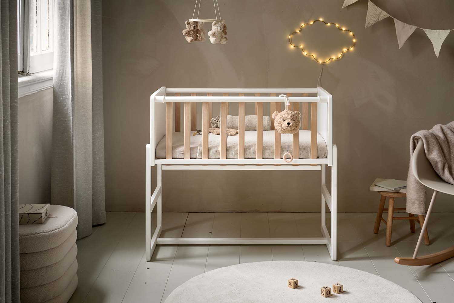 Weißes und naturfarbenes Beistellbett aus Holz in einem sanft eingerichteten Babyzimmer